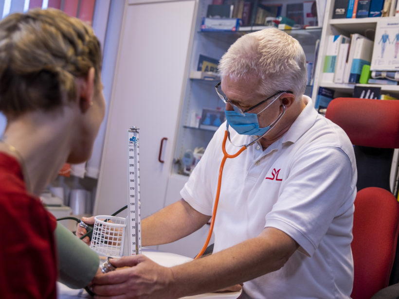 Arzt misst den Blutdruck bei einer Patienten in einem der Behandlungszimmer einer Hausarztpraxis.